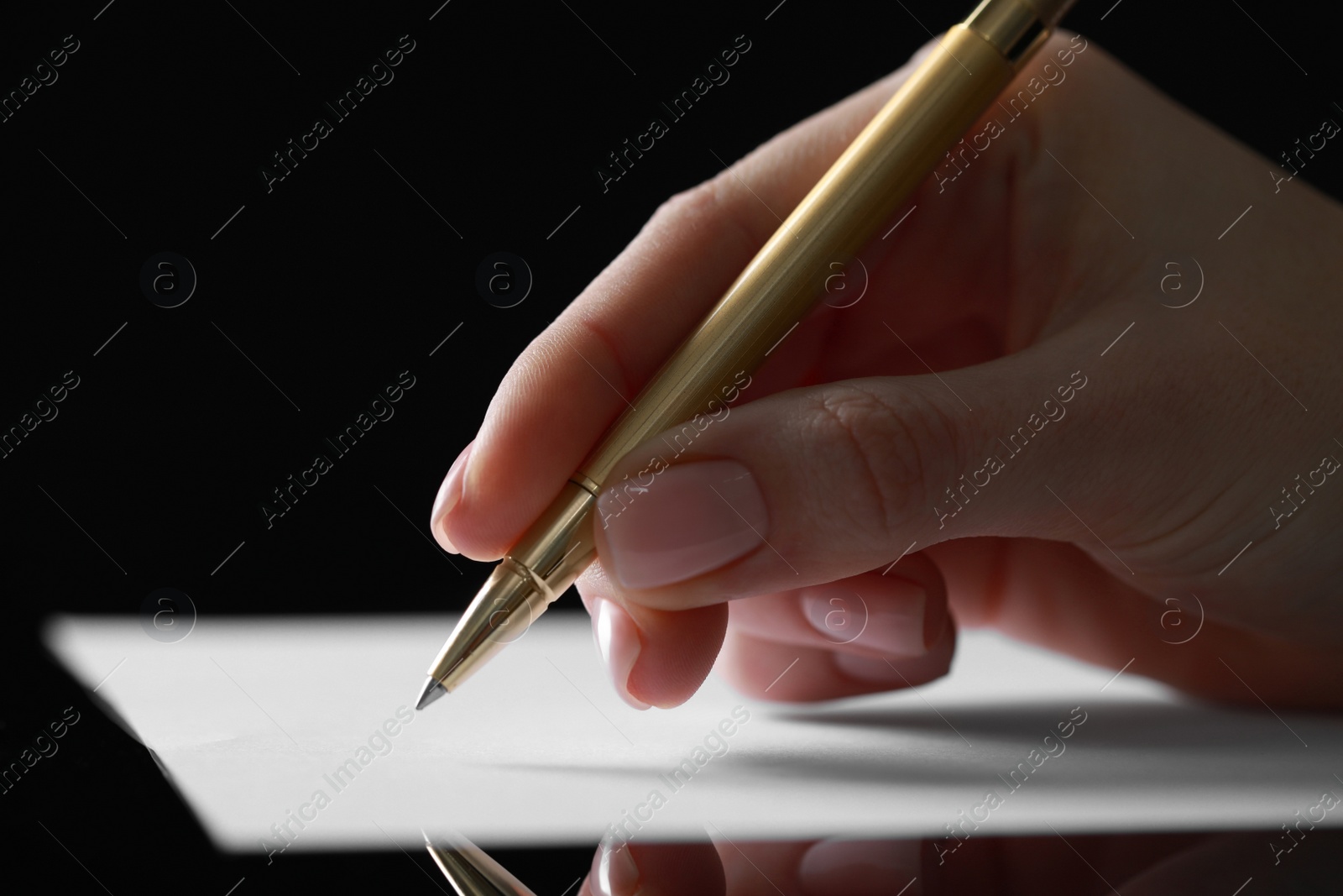 Photo of Woman writing on sheet of paper at glass table, closeup