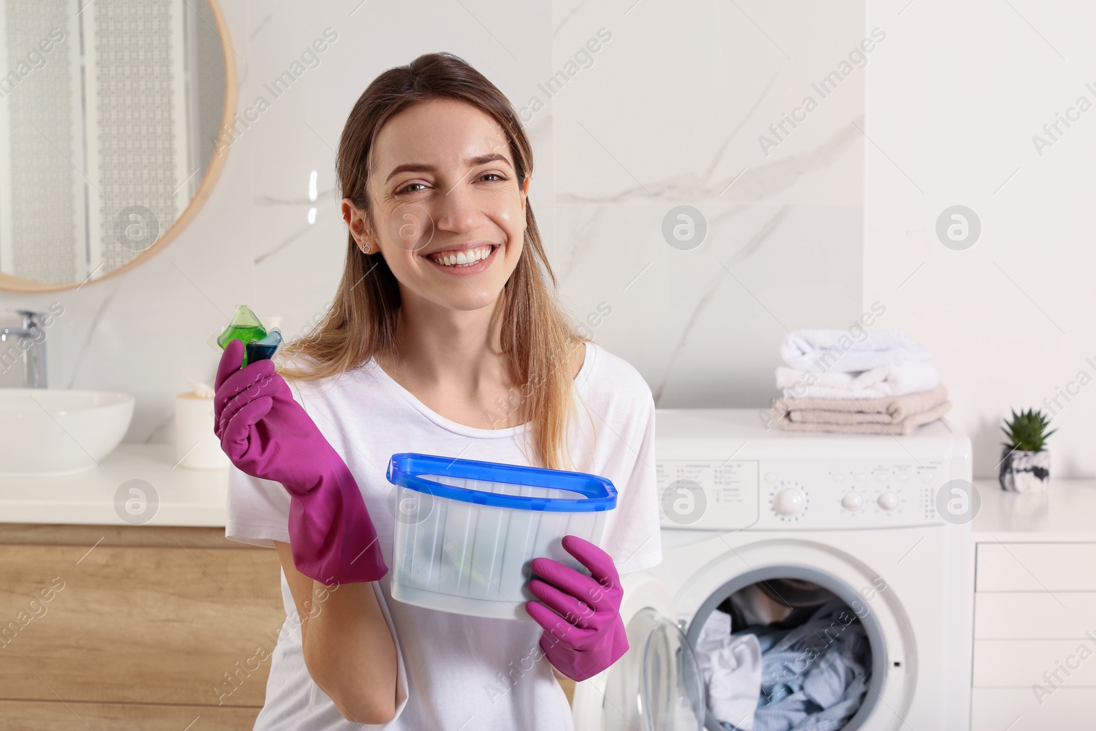 Photo of Woman holding container with laundry detergent capsules in bathroom