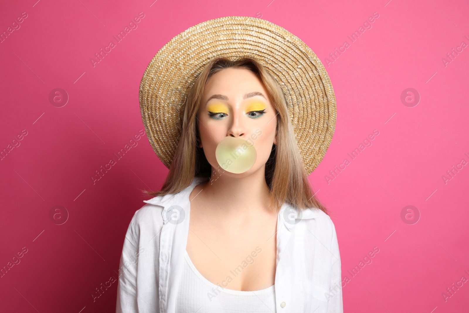 Photo of Fashionable young woman with bright makeup blowing bubblegum on pink background