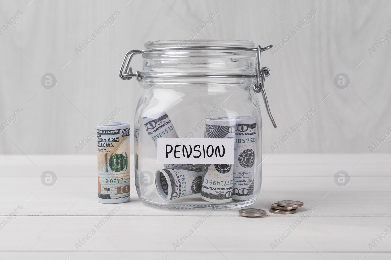 Photo of Glass jar with word Pension, coins and dollar banknotes on white wooden table