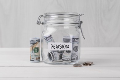 Photo of Glass jar with word Pension, coins and dollar banknotes on white wooden table