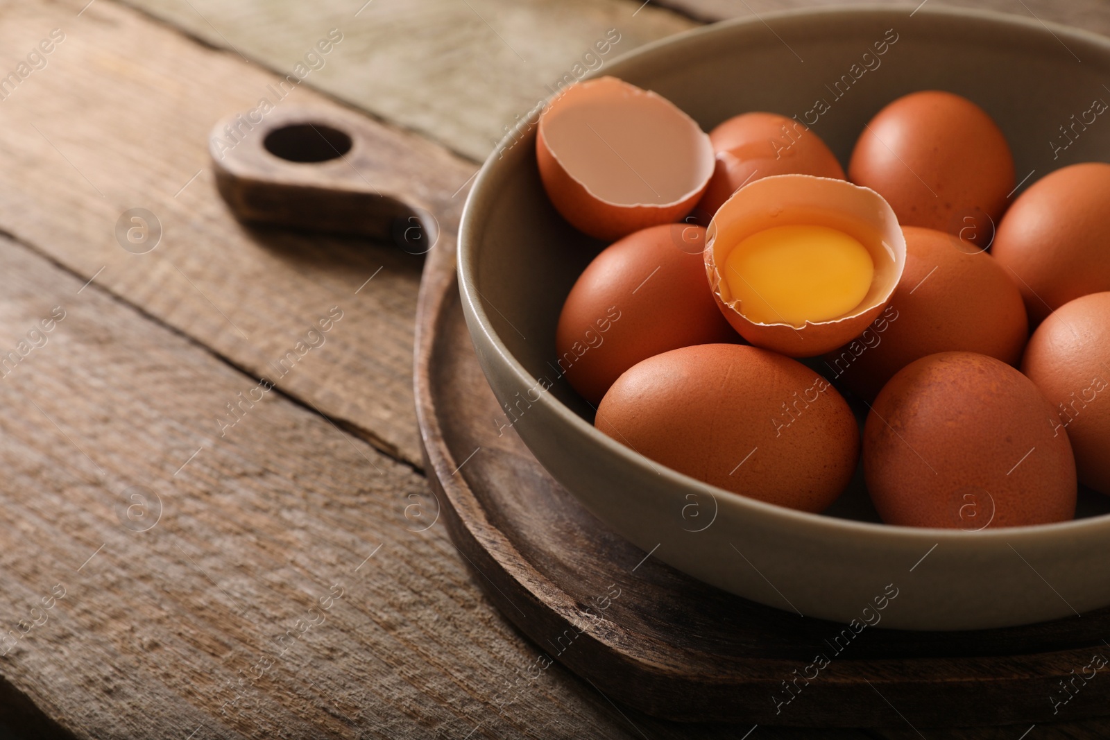 Photo of Bowl with raw chicken eggs on wooden table, closeup. Space for text