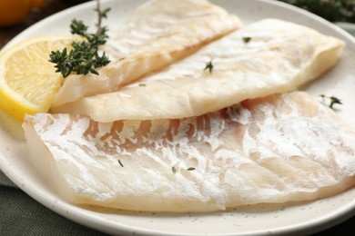 Photo of Fresh raw cod fillets with thyme and lemon on table, closeup