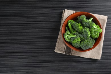 Bowl with fresh raw broccoli on black wooden table, top view. Space for text