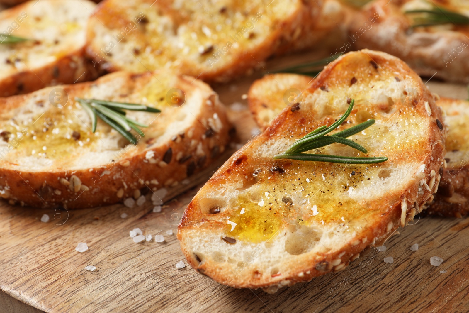 Photo of Tasty bruschettas with oil and rosemary on wooden board, closeup