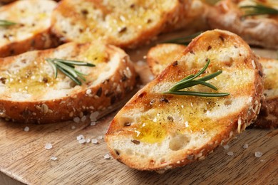 Photo of Tasty bruschettas with oil and rosemary on wooden board, closeup