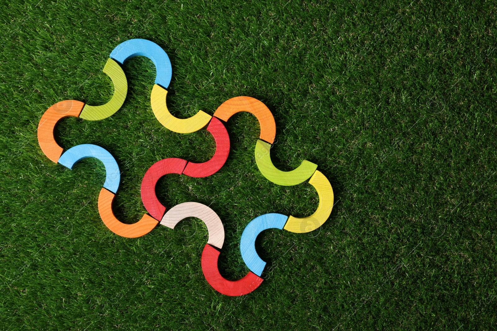 Photo of Colorful wooden pieces of play set on green grass, top view with space for text. Educational toy for motor skills development