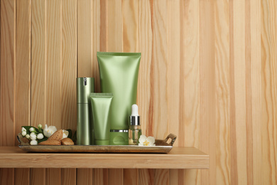 Photo of Set of cosmetic products, almond nuts and flowers on shelf near wooden wall, space for text