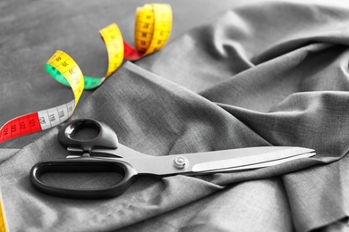 Scissors, fabric and measuring tape for tailoring on grey table