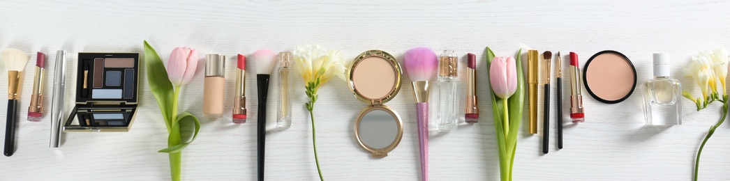 Photo of Flat lay composition with different decorative cosmetics and flowers on wooden table. Trendy makeup products