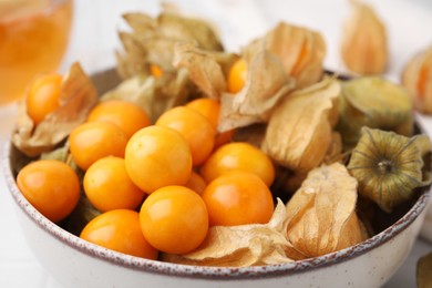 Photo of Ripe physalis fruits with calyxes in bowl on table, closeup
