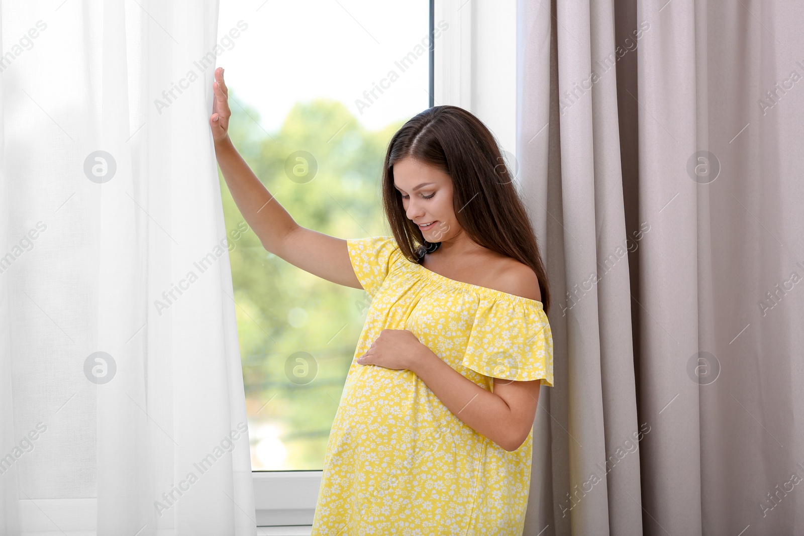 Photo of Happy pregnant woman standing near window at home