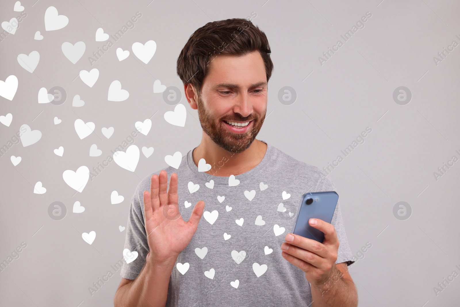 Image of Long distance love. Man video chatting with sweetheart via smartphone on grey background. Hearts flying out of device