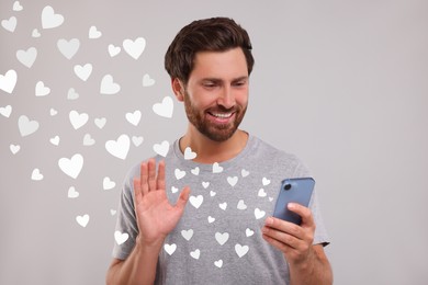 Long distance love. Man video chatting with sweetheart via smartphone on grey background. Hearts flying out of device