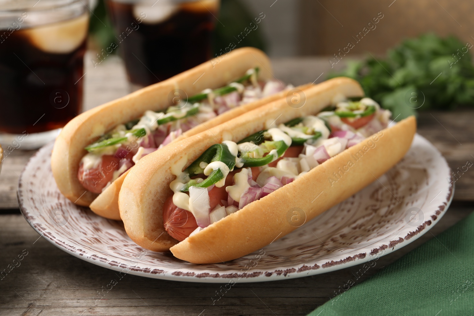 Photo of Delicious hot dogs with onion, chili pepper and sauce on wooden table, closeup