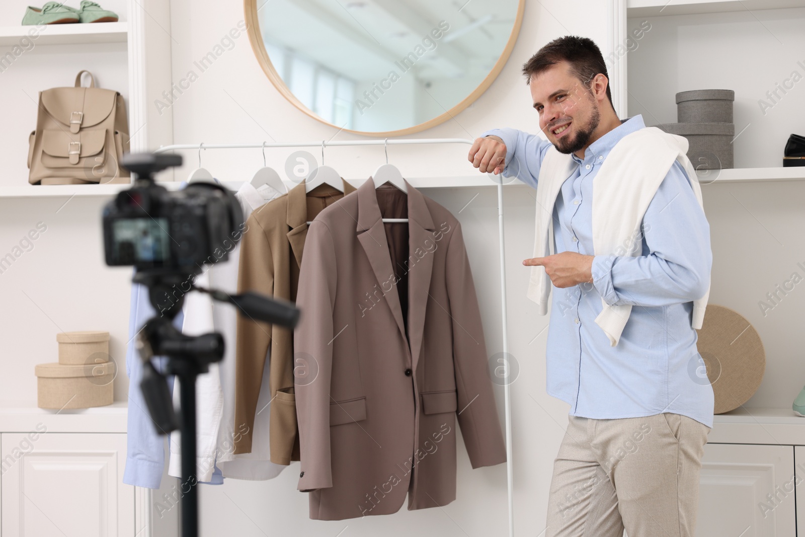 Photo of Smiling fashion blogger showing clothes while recording video at home