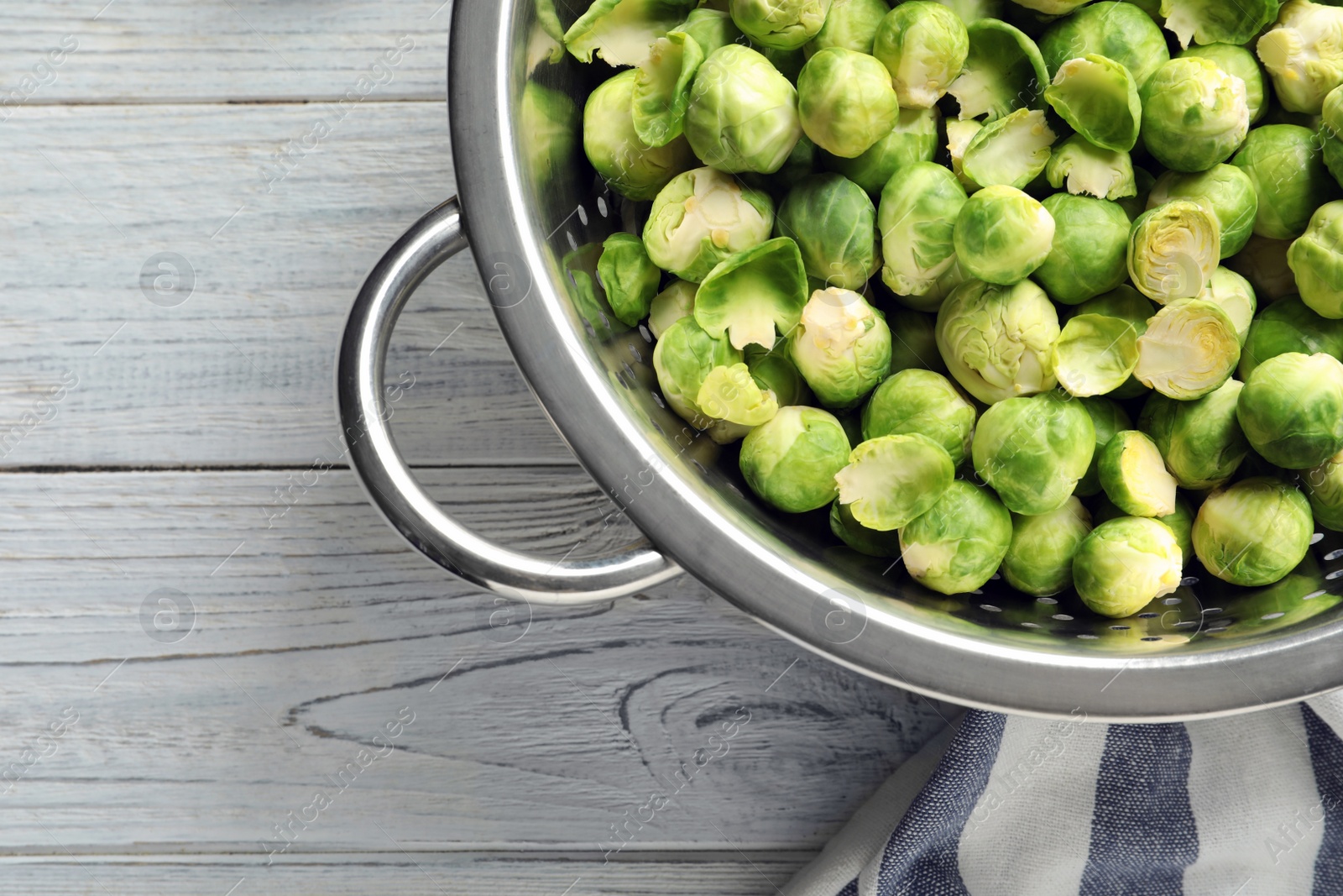 Photo of Colander with Brussels sprouts on wooden background, top view. Space for text