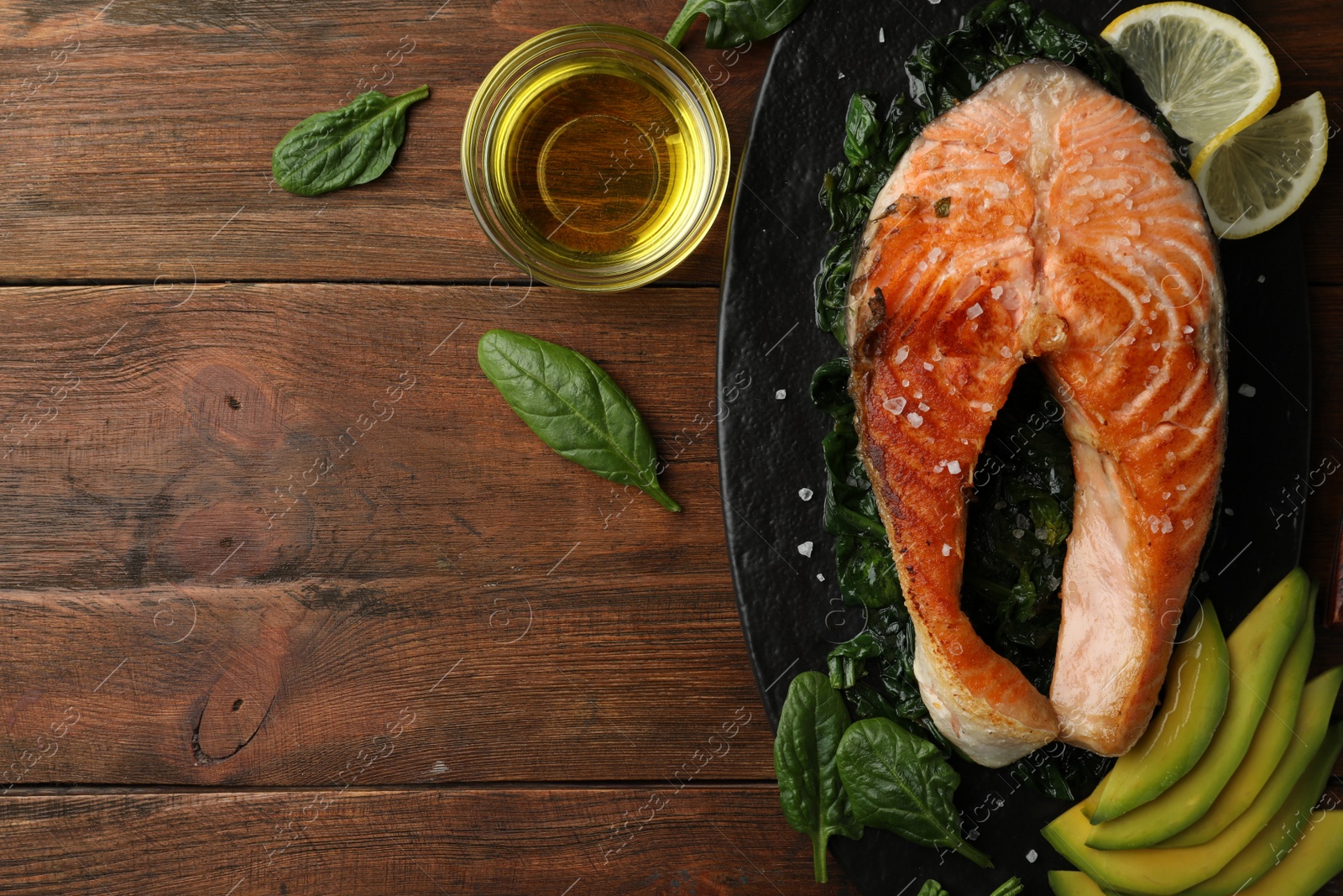 Photo of Tasty salmon with spinach served on wooden table, flat lay. Space for text