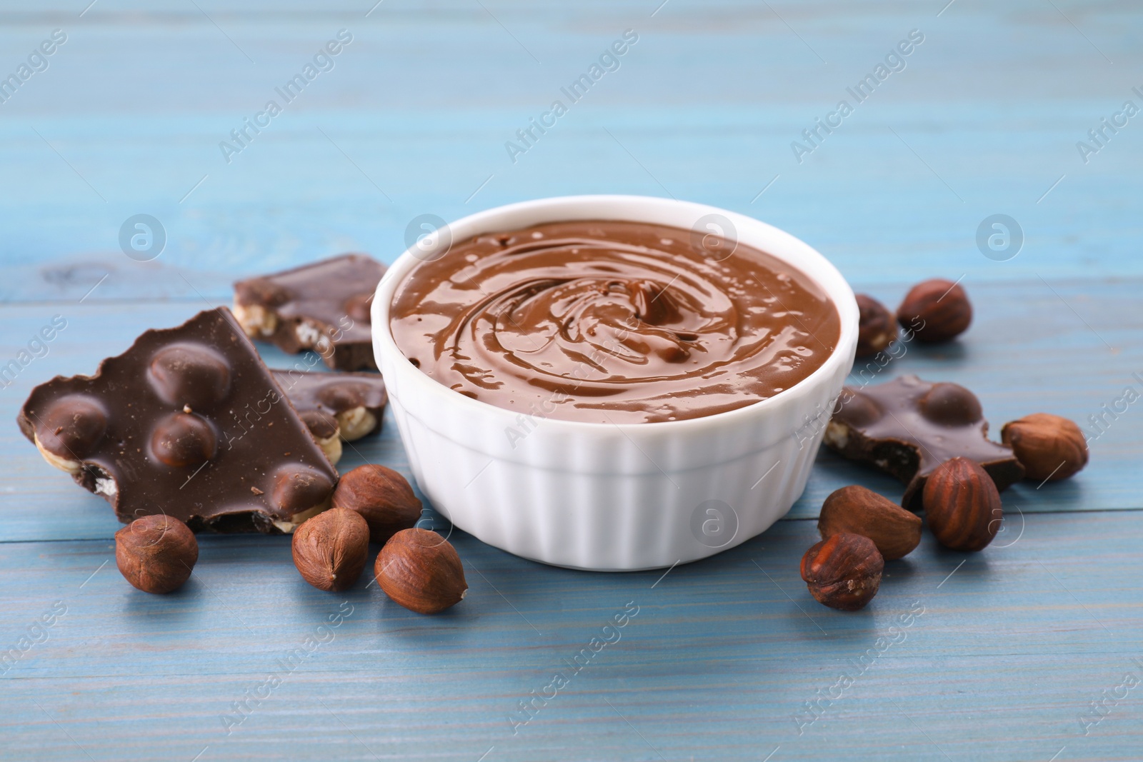 Photo of Bowl with tasty paste, chocolate pieces and nuts on light blue wooden table