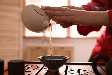 Photo of Master pouring freshly brewed tea into cup during traditional ceremony at table, closeup