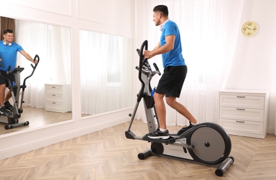 Photo of Man with headphones using modern elliptical machine at home