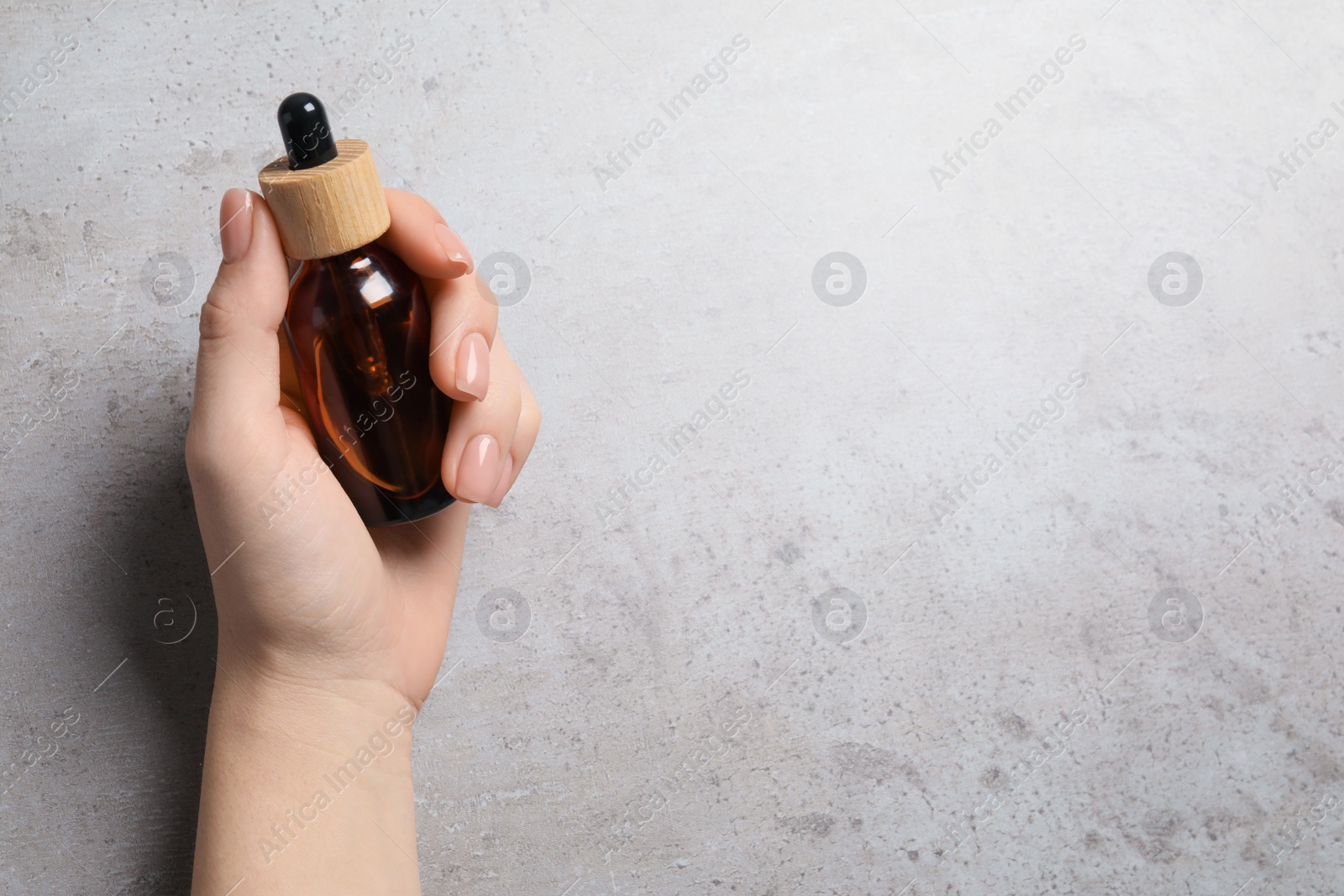 Photo of Woman holding bottle with serum at grey table, top view. Space for text