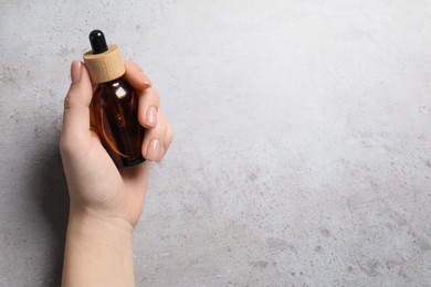 Photo of Woman holding bottle with serum at grey table, top view. Space for text