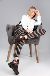Photo of Young stylish woman with trendy shoes sitting in armchair on grey background