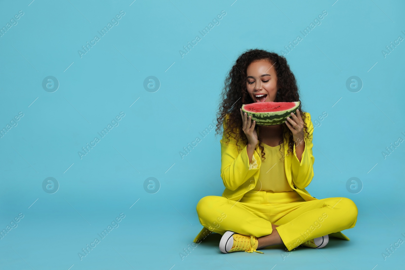 Photo of Beautiful young African American woman with watermelon on light blue background. Space for text