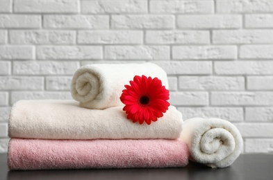 Photo of Rolled and folded soft towels with flower on table near brick wall