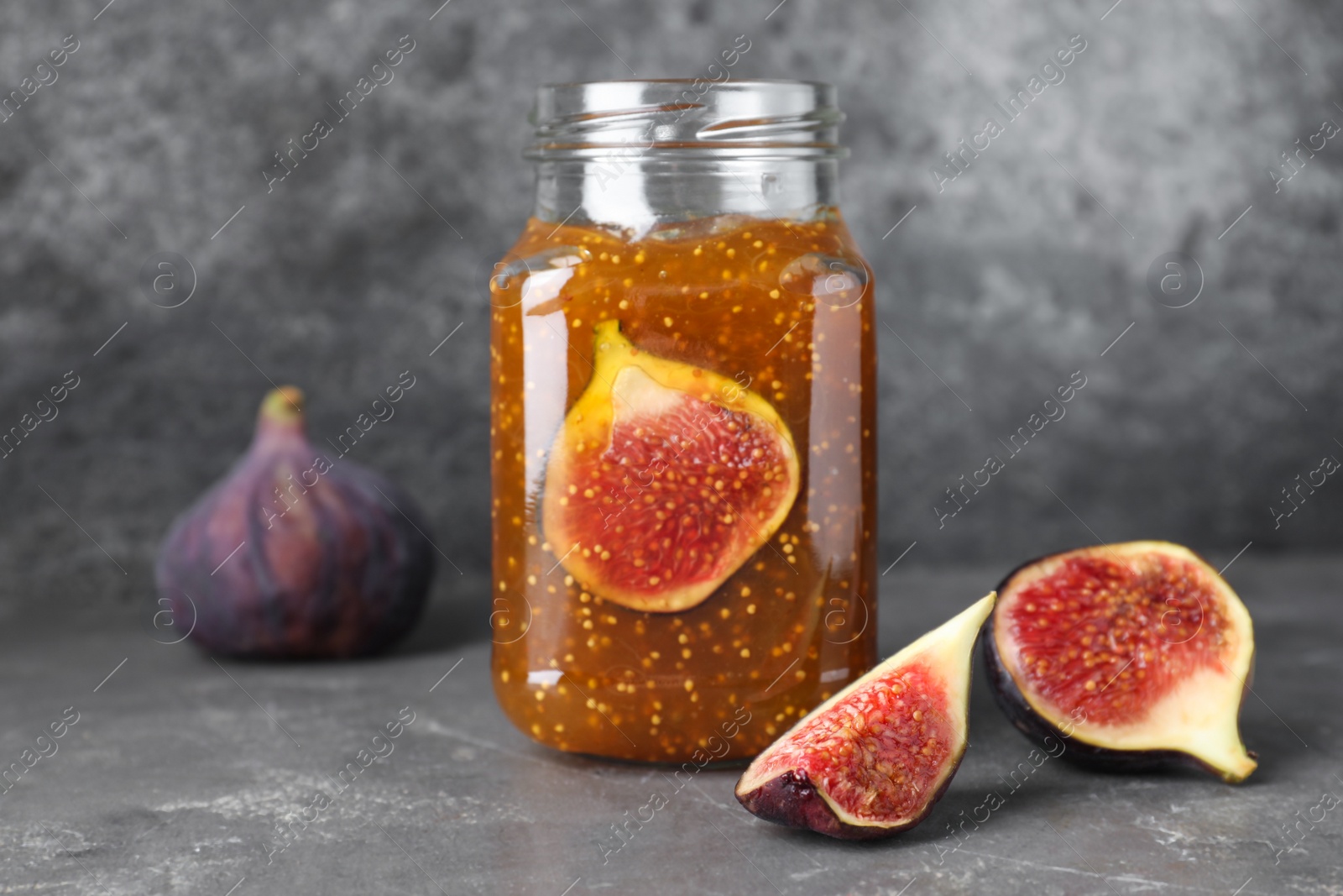 Photo of Delicious fig jam and fresh fruits on grey table