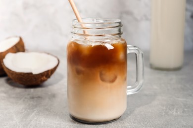 Mason jar of delicious iced coffee with coconut syrup on light grey table, closeup