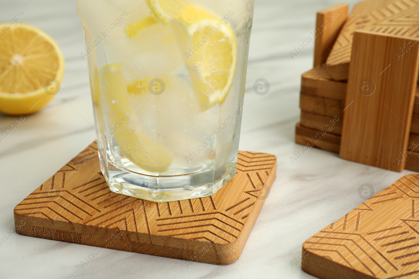 Photo of Glass of cocktail and stylish wooden cup coasters on white table