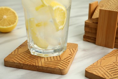 Photo of Glass of cocktail and stylish wooden cup coasters on white table