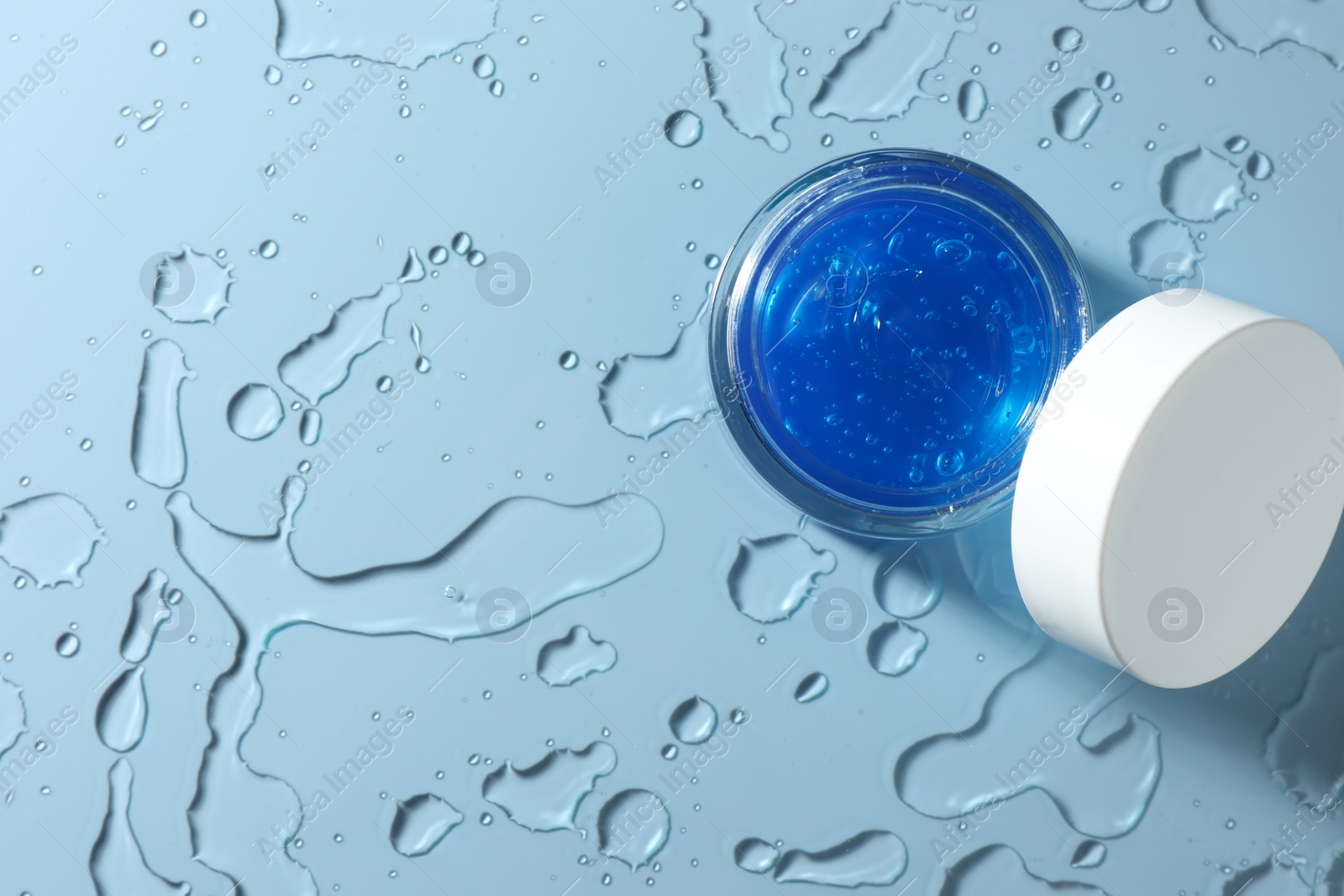 Photo of Open jar of cosmetic product and water drops on light blue background, top view. Space for text