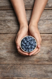 Photo of Woman holding juicy fresh blueberries on wooden table, top view
