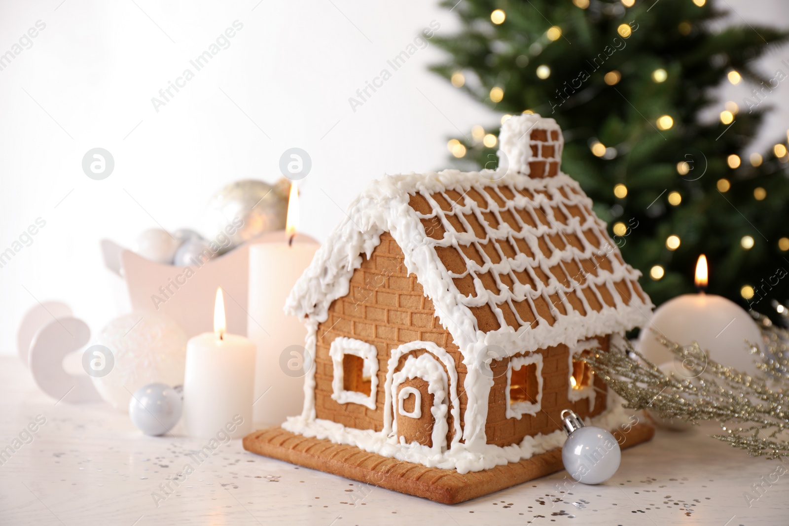 Photo of Beautiful gingerbread house decorated with icing and candles on white table