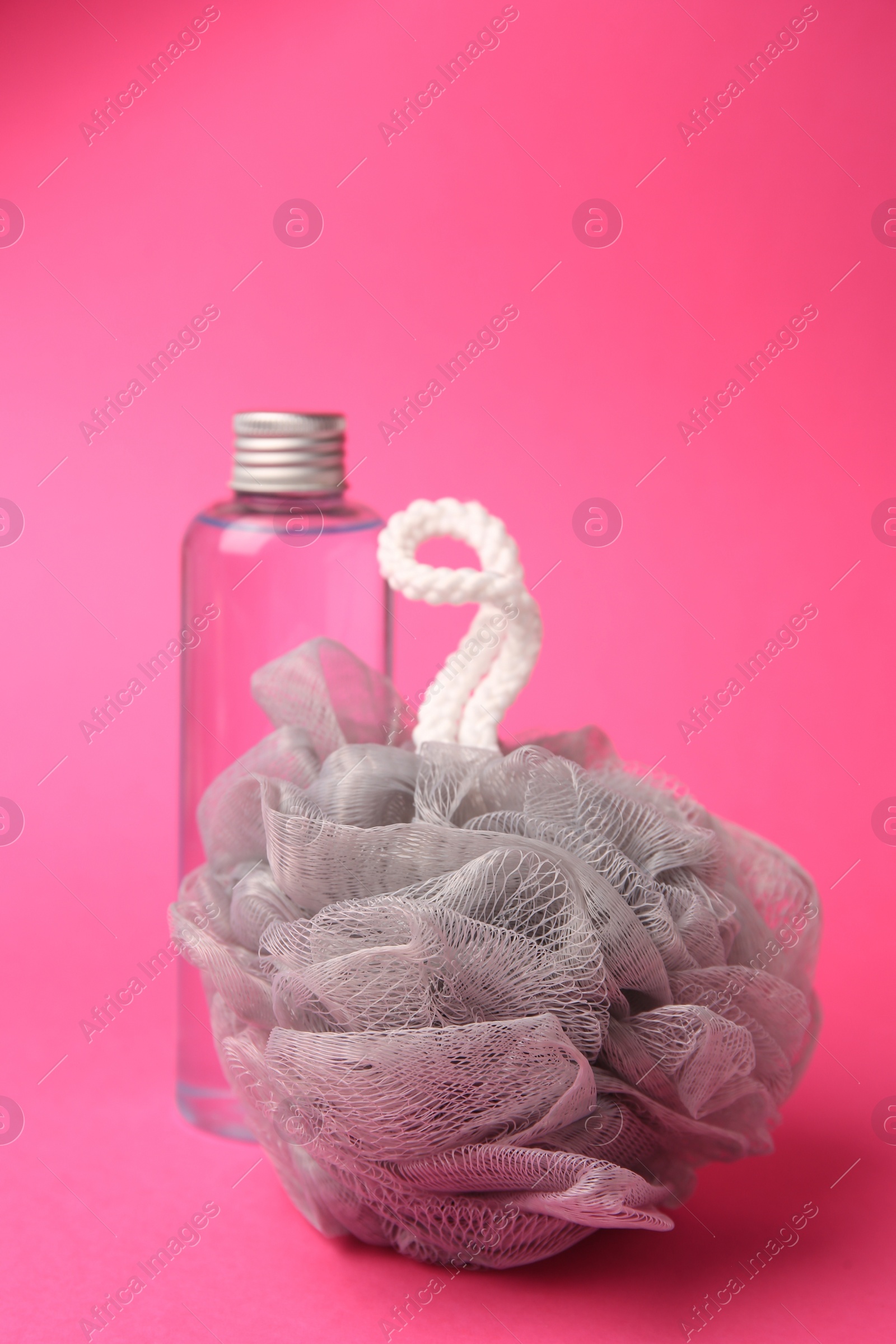 Photo of Grey shower puff and bottle of cosmetic product on pink background
