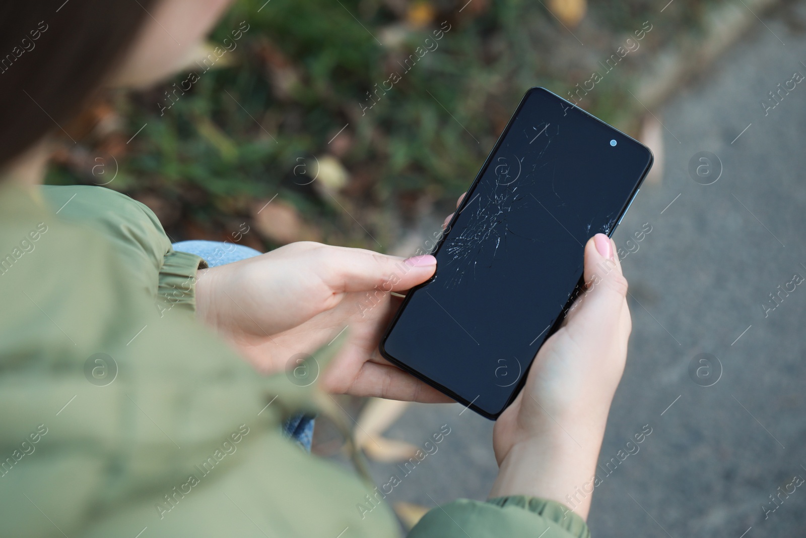 Photo of Woman holding damaged smartphone outdoors, closeup. Device repairing