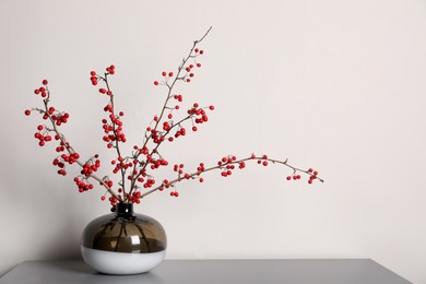 Photo of Hawthorn branches with red berries in vase on grey table indoors, space for text