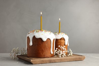 Tasty Easter cakes with burning candles on grey table