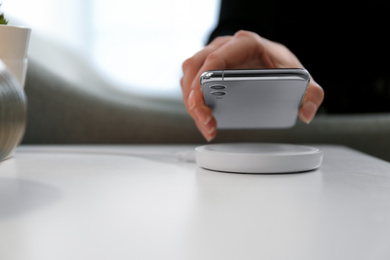 Photo of Woman putting smartphone on wireless charger in room, closeup. Space for text