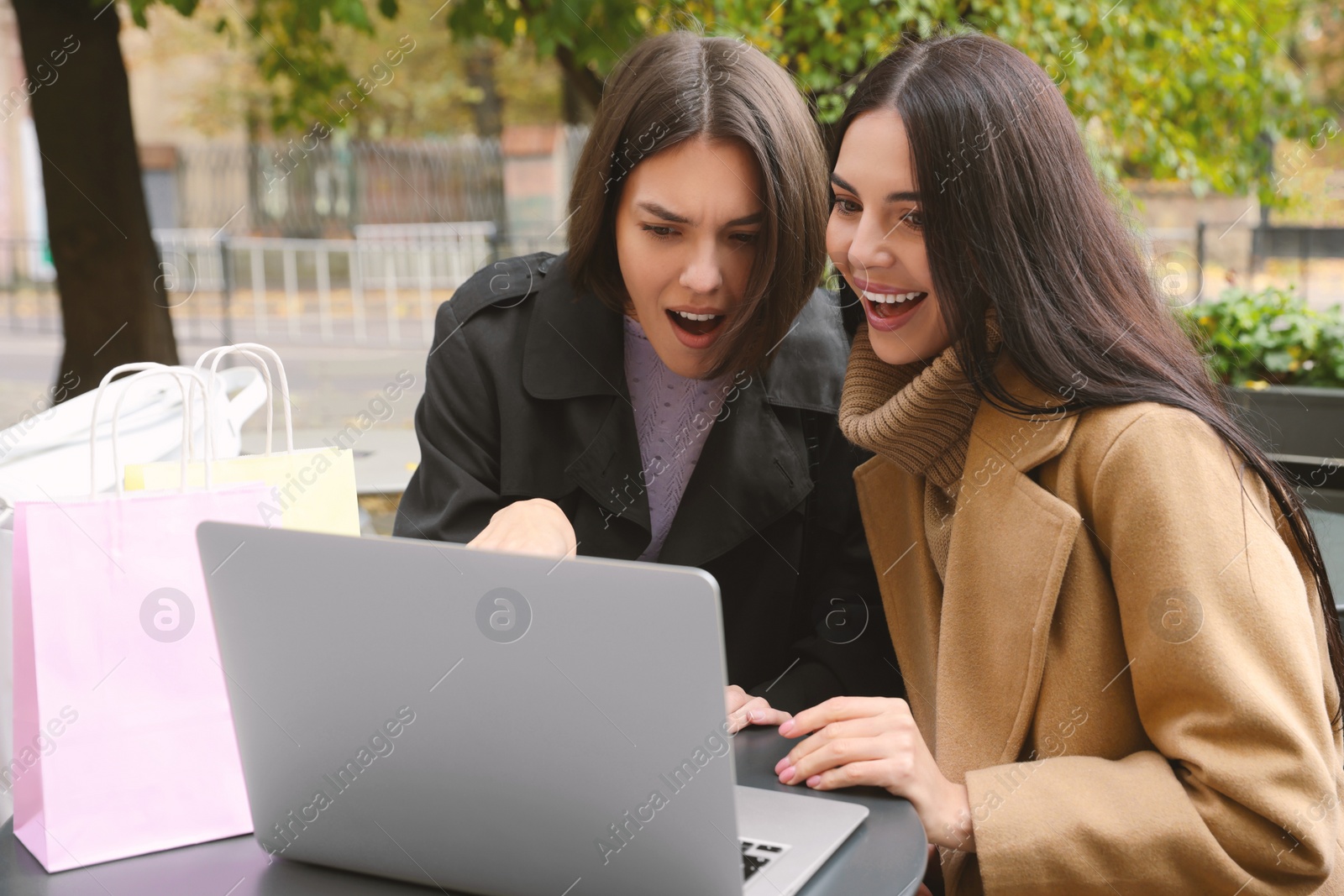 Photo of Special Promotion. Emotional young women with shopping bags using laptop in outdoor cafe