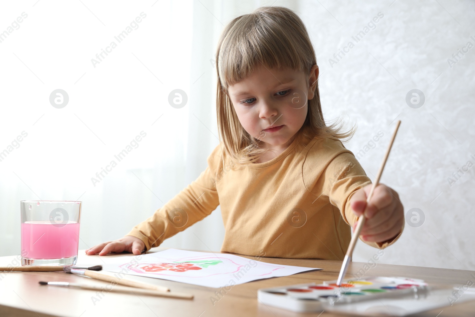 Photo of Cute little girl drawing with brush at wooden table indoors. Child`s art