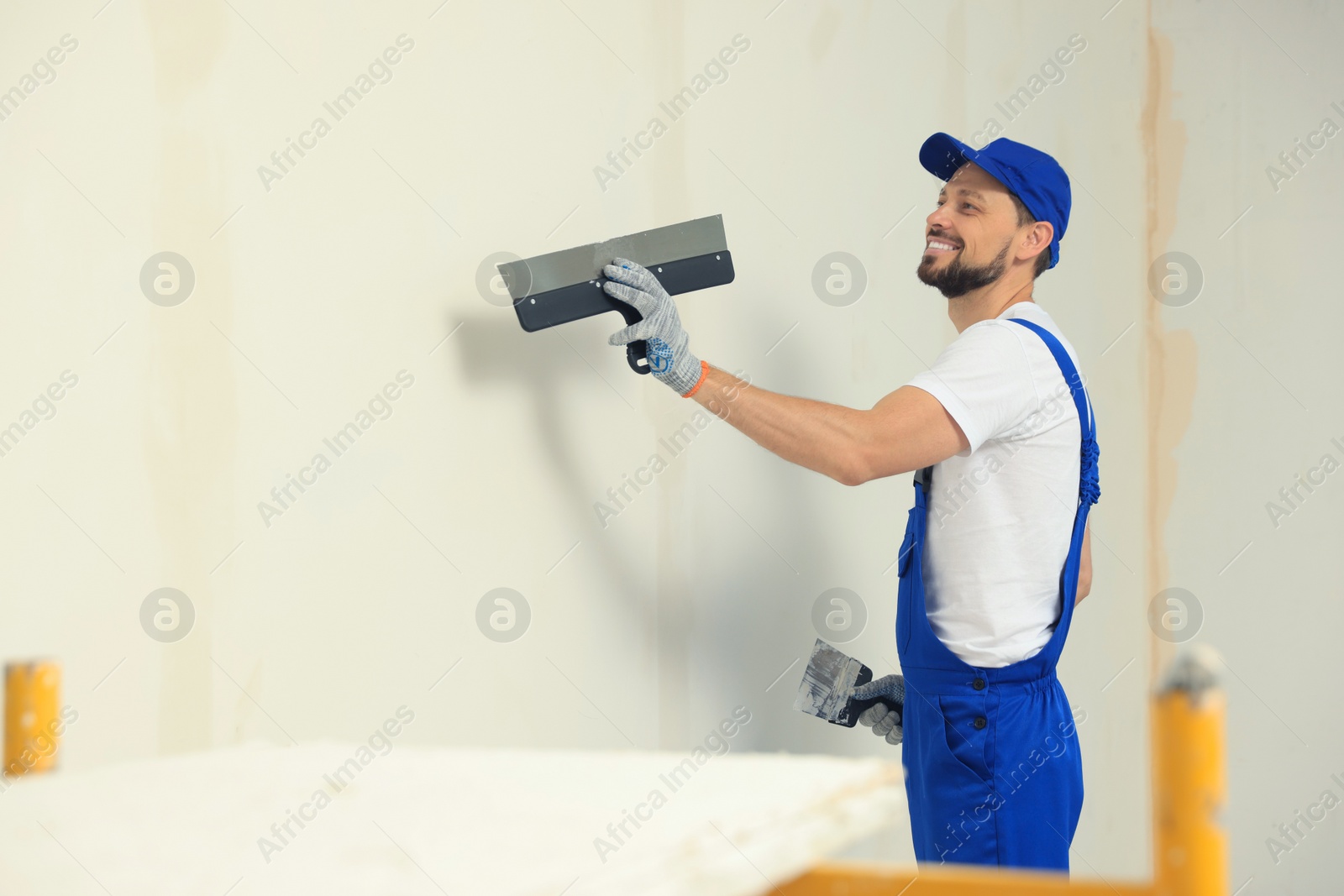 Photo of Professional worker plastering wall with putty knives indoors. Space for text