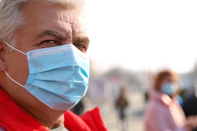 Senior man with medical mask on city street, space for text. Virus protection