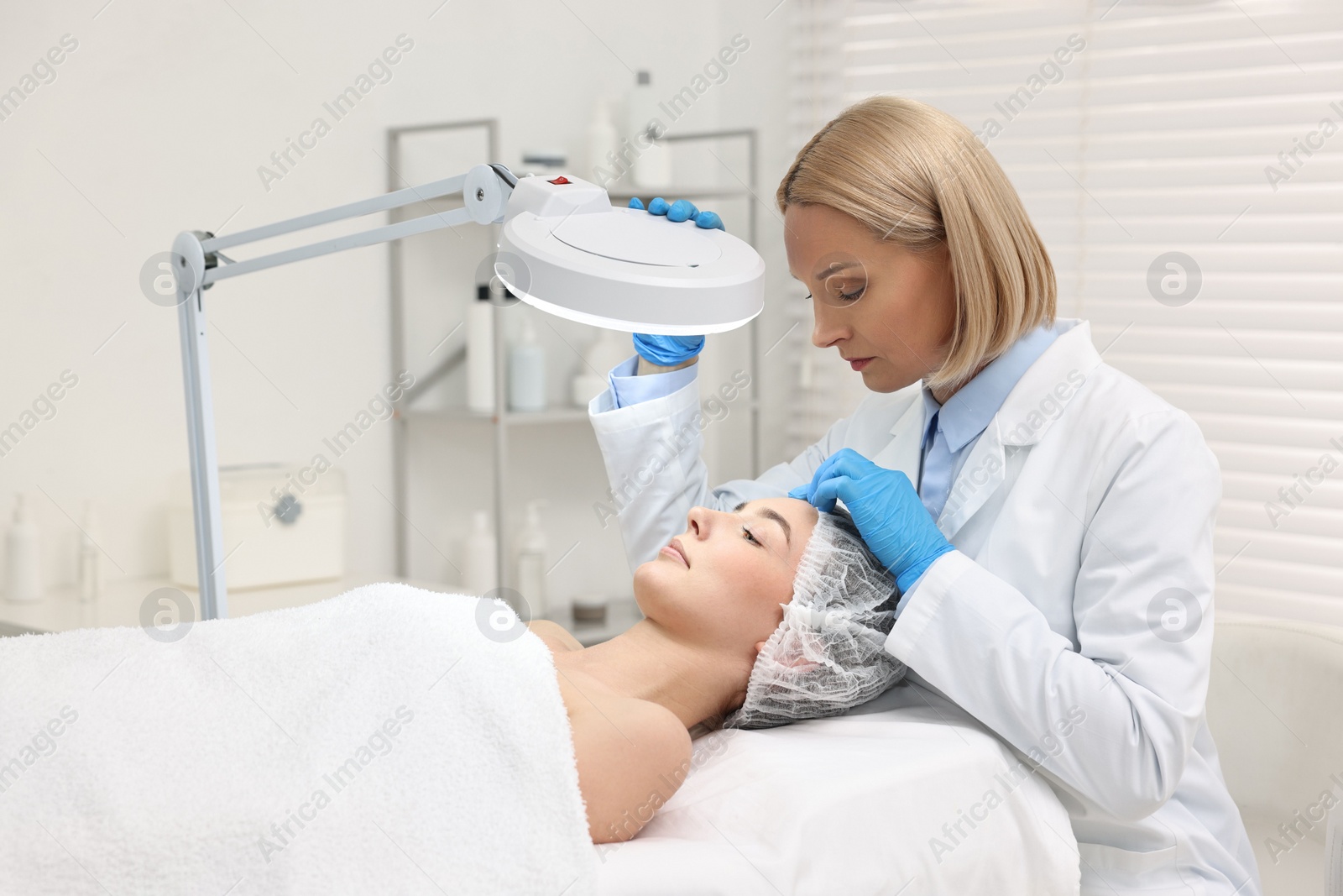 Photo of Dermatologist examining patient`s face under lamp in clinic