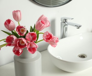 Photo of Vase with beautiful pink tulips and toiletries near sink in bathroom, closeup