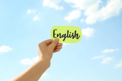 Photo of Woman holding sheet of paper with word English against blue sky, closeup