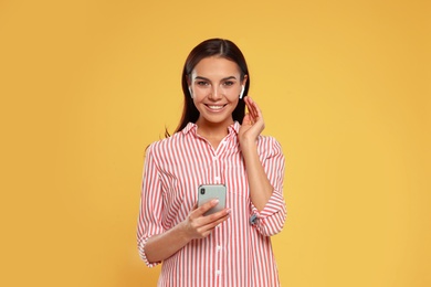 Photo of Happy young woman with smartphone listening to music through wireless earphones on yellow background